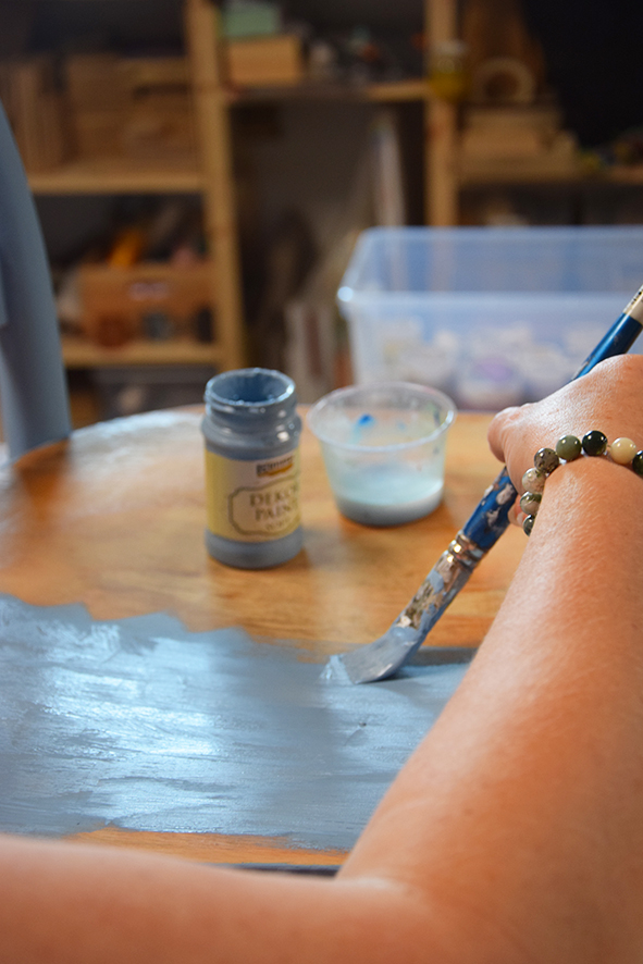 Žena natiera základ stoličky modrou Decor paint farbou.